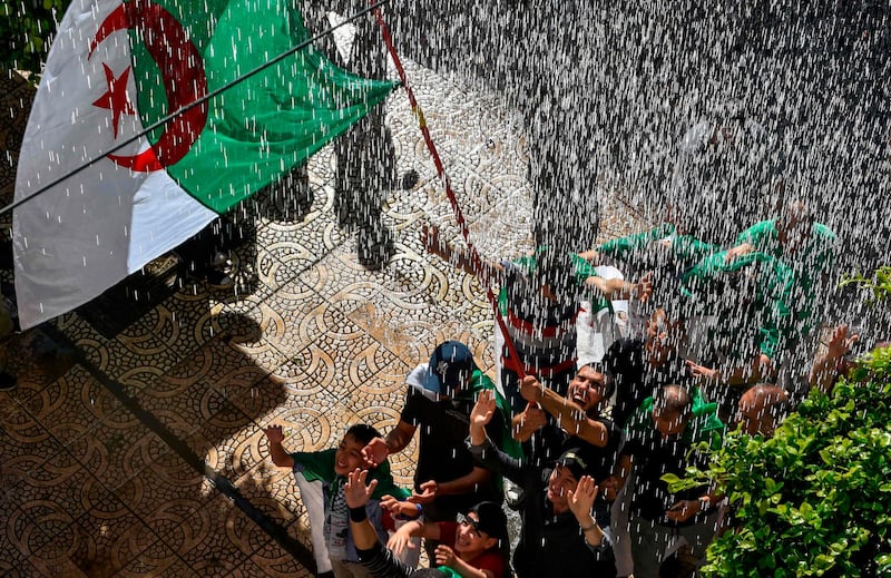 Algerian protesters wave a national flag beneath a shower of water in a street during an anti-government demonstration in the capital Algiers. AFP