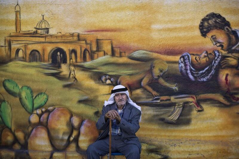 Palestinian refugee Abdul Ghafour Abdulrahman, 85, who witnessed  what the Palestinians call the “Nakba,” or “catastrophe” referring to their uprooting in the war over Israel’s 1948 creation, sits in front of a wall painted with a mural depicting the Israeli-Palestinian conflict in the Kalandia refugee camp, between Jerusalem and the West Bank city of Ramallah.