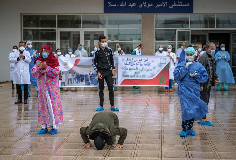 TOPSHOT - A patient who recovered from the Covid-19 disease caused by the novel coronavirus kisses the ground as another rejoices with the medical staff as they leave a hospital in the city of Sale, north of the Moroccan capital Rabat on April 12, 2020. / AFP / FADEL SENNA
