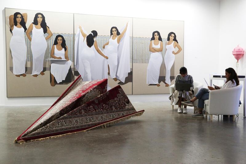Women sit in front of Egyptian artist Ibrahim el-Dessouki's 2019 painting "The Seventh Day" and near Lebanese artist Ali Chaaban's 2019 Persian carpet work called "12:00 p.m. Class" at Art Dubai in Dubai. AP Photo