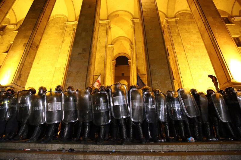 Police block an entrance of the Georgian Parliament as opposition demonstrators gather to call for the resignation of the speaker of the Georgian Parliament in Tbilisi, Georgia, Friday, June 21, 2019. Police have fired a volley of tear gas at a massive throng of protesters outside the Georgian national parliament, who are trying to storm the building and are demanding the government's resignation.(AP Photo/Zurab Tsertsvadze)