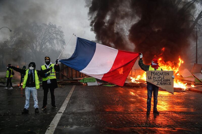 Protesters hold a French flag near a burning barricade during a protest of Yellow vests in Paris. AFP