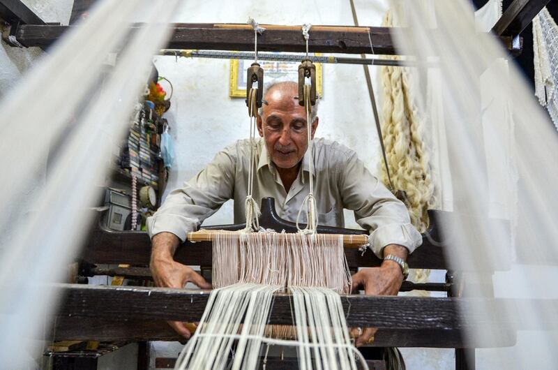 Muhammad Saud, a 65-year-old Syrian silk farmer, handweaves silk threads on a loom at his home workshop in the village of Deir Mama, in west-central Syria.  AFP