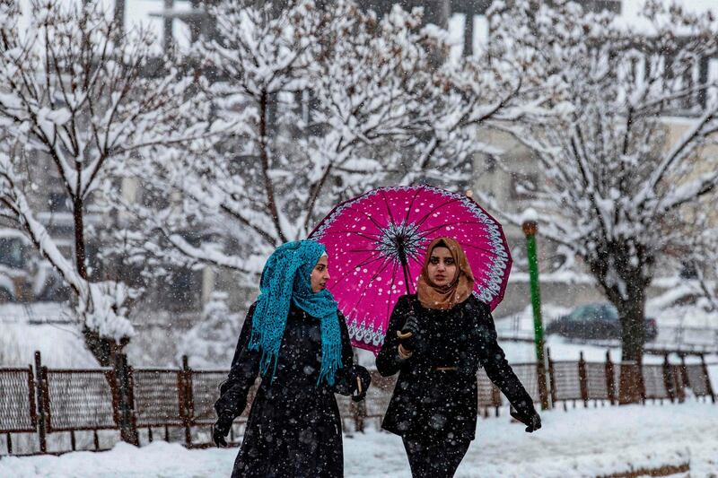 Women walk under an umbrella along the side of a snow-covered street in the northeastern Syrian town of Al Malikiyah at the border with Turkey during a blizzard.  AFP