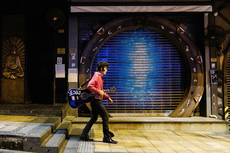 This photo taken on March 23, 2020 shows Kwok Lam-sang, 67, who has been performing covers of Elvis Presley songs under the name of "Melvis" since 1992, walking with his guitar past closed bars in the usually busy drinking area of Lan Kwai Fong in Hong Kong, after restaurants and bars in the city were banned from selling alcohol as a preventive measure against the spread of the COVID-19 novel coronavirus. / AFP / Anthony WALLACE
