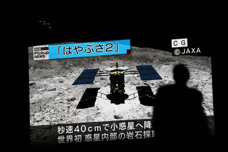 In this picture taken on July 10, 2019 a man walks past a screen displaying a computer-generated image of the Hayabusa2 probe, during a news broadcast at Akihabara district in Tokyo. Japan's Hayabusa2 probe landed successfully on a distant asteroid for a final touchdown on July 11, 2019, hoping to collect samples that could shed light on the evolution of the solar system.
 / AFP / Behrouz MEHRI
