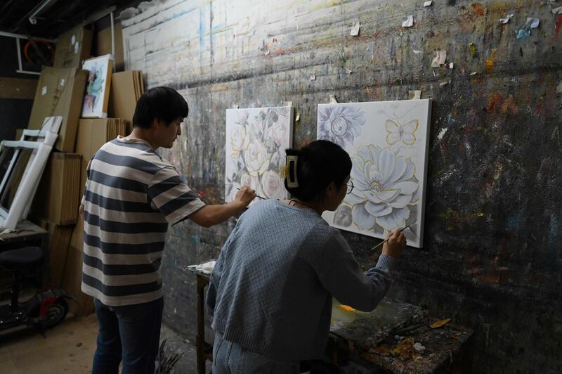 Artists paint on top of pre-printed art works in a workshop 