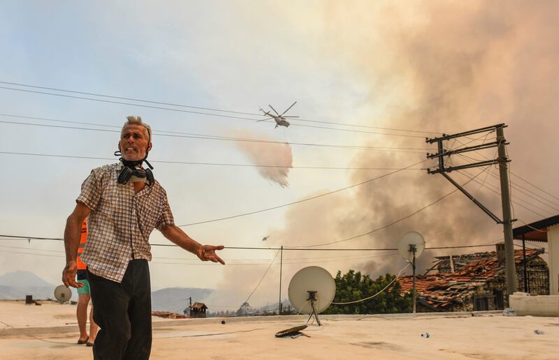 A man reacts as a helicopter pours water over Sirtkoy, a village near Manavgat.