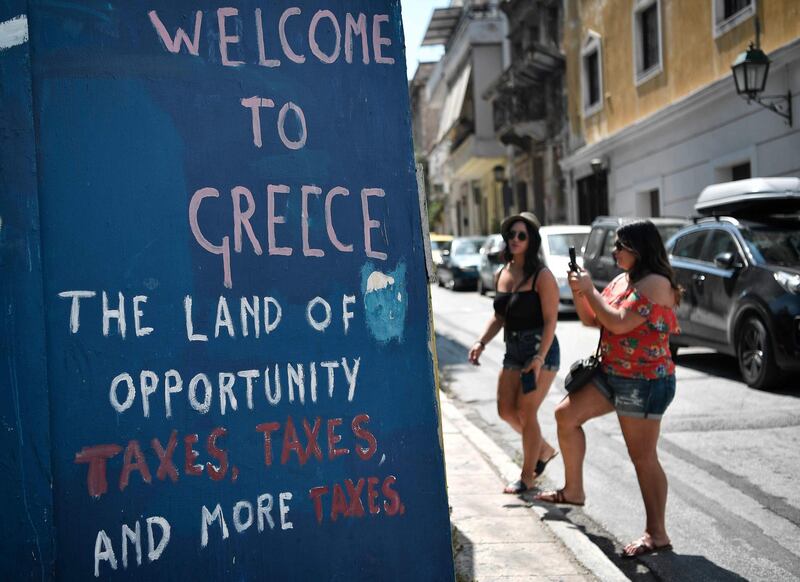 Tourists take pictures of slogans on a wall in central Athens, on August 18, 2018. - On August 20, Greece's third and final bailout officially ends after years of hugely unpopular and stinging austerity measures. The economy is growing slowly, and unemployment fell to below 20 percent in May for the first time since 2011. (Photo by LOUISA GOULIAMAKI / AFP)