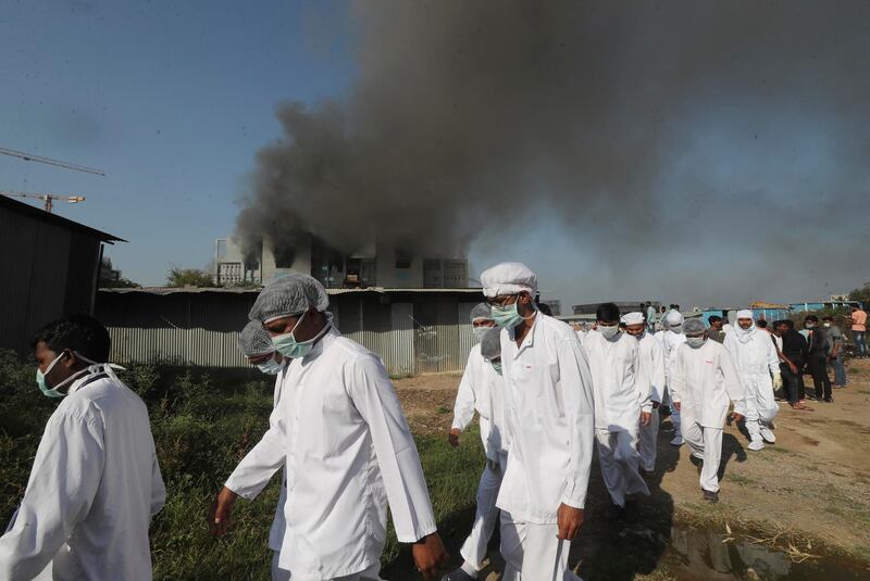 Employees leave as smoke rises from a fire at Serum Institute of India. AP Photo