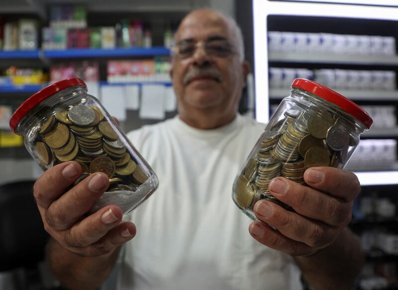 Antoine Saab with two jars full of Lebanese pound coins at his shop in Beirut.