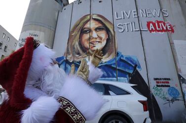 A man dressed a a Santa outfit poses next to a mural of slain US-Palestinian correspondent Shireen Abu Akleh is pictured at a section of Israel's separation wall in the biblical West Bank city of Bethlehem on December 22, 2022, ahead of Christmas.  (Photo by HAZEM BADER  /  AFP)