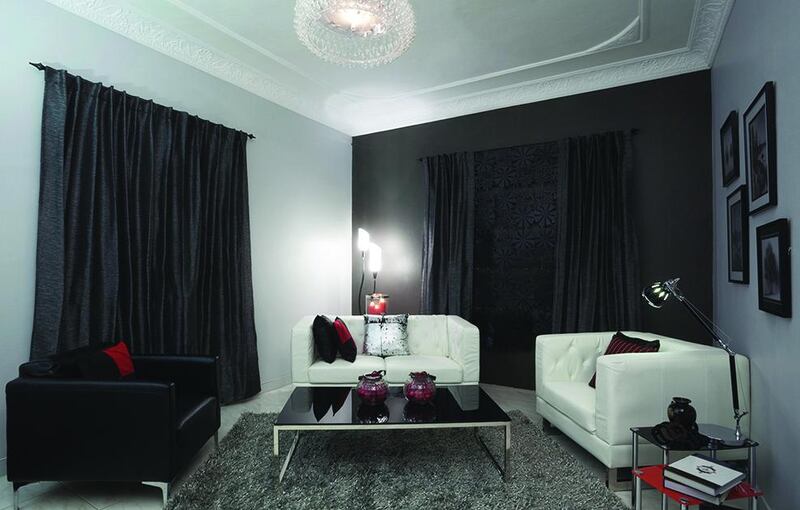 AFTER — Stylist solutions: In this instance, a balcony had been closed off from the outside to create a storage room, which blocked out any natural light. Masoud and his wife wanted to modernise the space and introduce a monochromatic colour palette, interspersed with pops of red. First off, the stylist had to hide the doorway to the balcony. The walls were painted light grey with one dark grey wall as an accent wall. The stylist added Oxford floor lamps, a Ranmak ceiling lamp and lots of filled cushions to give the room a burst of life compensated for the lack of natural light coming into the room.