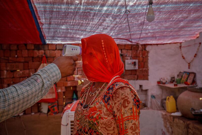 A healthcare worker checks the temperature of a woman inside her hut during a coronavirus disease vaccination drive in Kavitha village on the outskirts of Ahmedabad, India, on April 8, 2021. By Amit Dave, Pulitzer Prize Winner for Feature Photography. Reuters