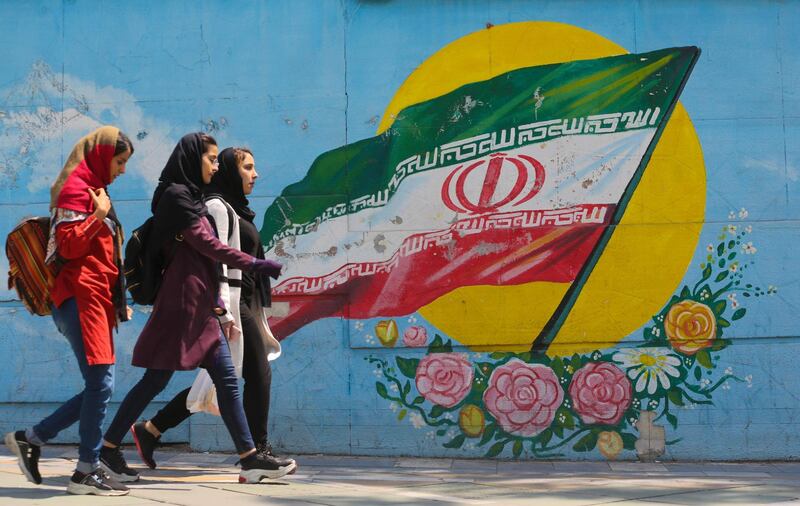 Young girls walk in front of a mural showing the Iranian national flag in the centre of the  capital Tehran, on April 23, 2019.  The White House announced yesterday it was calling an end to six-month waivers that had exempted several countries from unilateral US sanctions on Iranian oil exports. / AFP / ATTA KENARE
