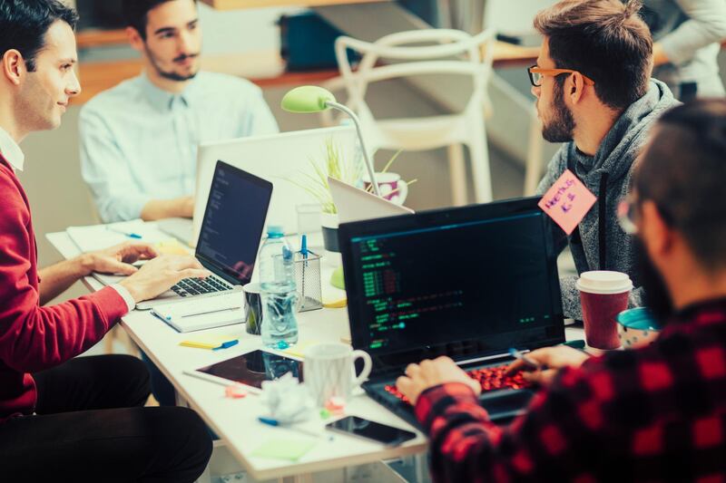 Five young people running their coding startup company. Working from the house like business incubator. Sitting and collaborating. Using their laptops for coding. Selective focus to young man with glasses talking to his coworker. Shot with Canon EOS 5Ds. Getty Images