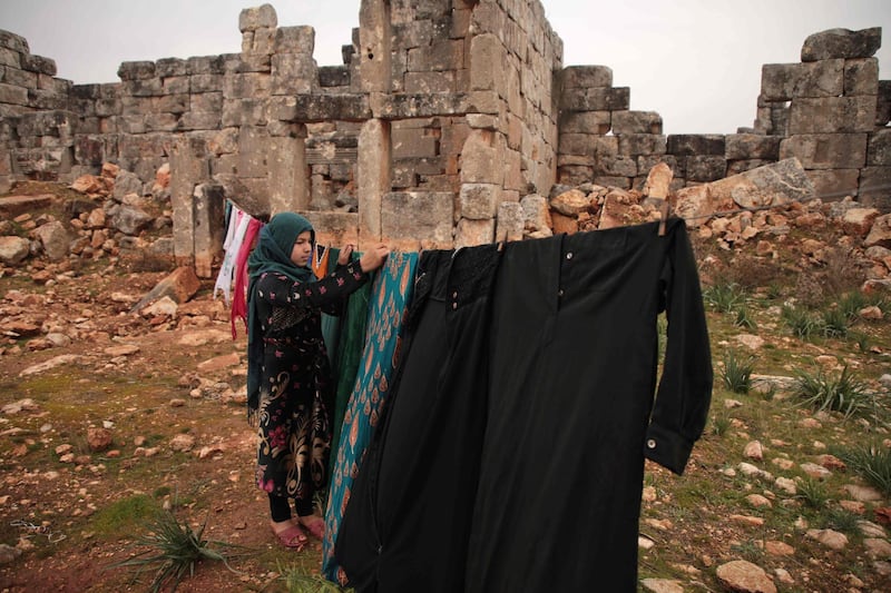 A Syrian girl, displaced from the western countryside of Aleppo province, hangs laundry out to dry by an encampment at the site of ancient ruins for refuge from the rain, near the town of Atareb.   AFP