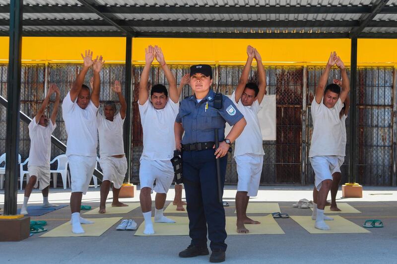 Nicol Gomez, a guardian at the La Esperanza prison, poses for a portrait in front a group of prisoners practising yoga in San Salvador.  Marvin Recinos / AFP Photo
