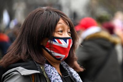 A woman wears a Union flag themed face mask as an anti-lockdown demonstration takes place in Parliament Square, in London, Monday, Dec. 14, 2020. Britain launched its vaccination program this month after becoming the first country to give emergency approval to the Pfizer-BioNtech vaccine, and authorities plan to dispense 800,000 doses in the first phase. (AP Photo/Alberto Pezzali)