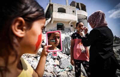 A Palestinian woman paints a national flag on the face of a child as another looks in a mirror, amidst the rubble of buildings destroyed by last month's Israeli bombardment of the Gaza Strip, in Beit Lahia, in the northern part of the Palestinian enclave, on June 19, 2021. / AFP / MAHMUD HAMS
