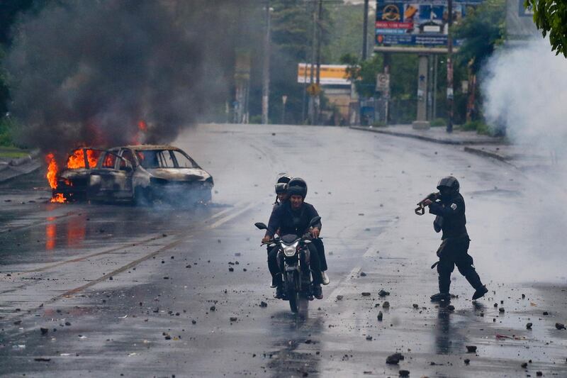 A police officer aims his shotgun at two men riding a motorcycle during a protest against Nicaragua's President Daniel Ortega in Managua, Nicaragua. Esteban Felix / AP Photo