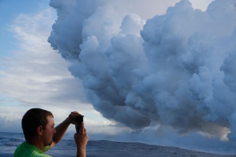 Joe Kekedi takes pictures of a plume of steam as lava enters the ocean near Pahoa, Hawaii. Kilauea volcano that is oozing, spewing and exploding on Hawaii's Big Island has gotten more hazardous in recent days, with rivers of molten rock pouring into the ocean Sunday and flying lava causing the first major injury. Jae C. Hong / AP Photo