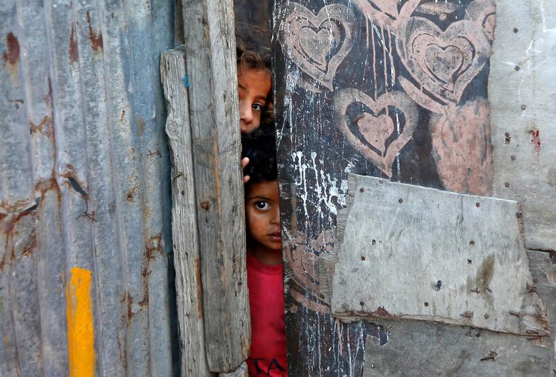 Palestinian children peep from behind a makeshift door at an empoverished neighbourhood in Gaza City on July 4, 2019. / AFP / MOHAMMED ABED
