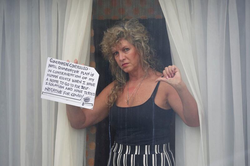 A quarantined traveller holds a sign up to the window of her room at the Radisson Blu Edwardian hotel.