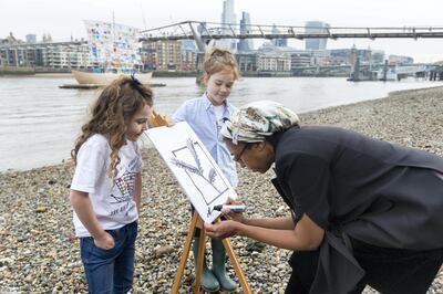 Nadja Romain, founder of Art Action Change signs a panel on the shore of the river Thames with contributing artists left Esmeralda and Sholto. Mark Chilvers for The National