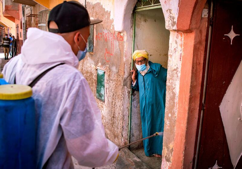 A man confined at home watches as a Moroccan municipal worker disinfects his street in the southern port city of Safi on June 9, 2020, during a lockdown ordered by the authorities following the detection of several new cases of Covid-19.  AFP