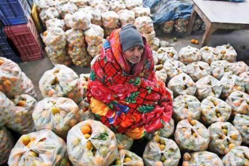 A vendor wrapped in a quilt sits on his bags of oranges as he waits for customers at a wholesale market in the northern Indian city of Chandigarh.