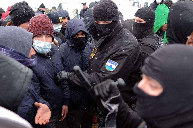 Bosnian police stand in front of migrants waiting in lines for food handouts during snowfall at the Lipa camp. AP Photo