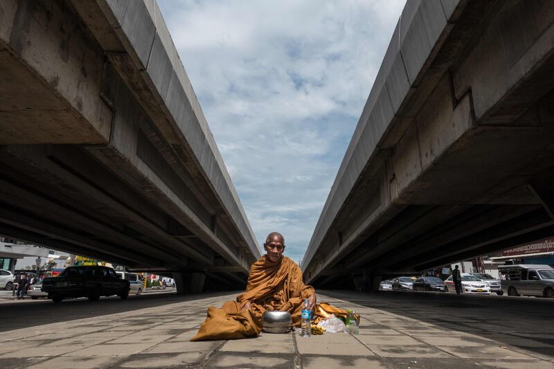 A Buddhist monk sits between two overpasses as he waits to receive alms in northern Bangkok. Jerome Taylor / AP Photo