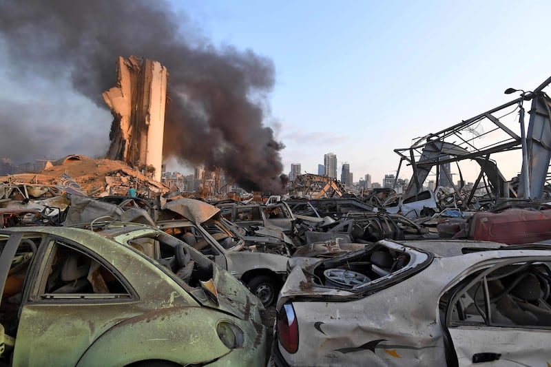 Damaged cars are pictured in front of billowing smoke behind the grain silos at the port of Beirut. AFP