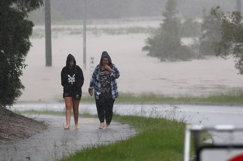People walk in rain near a flooded road in the city of Logan.   EPA