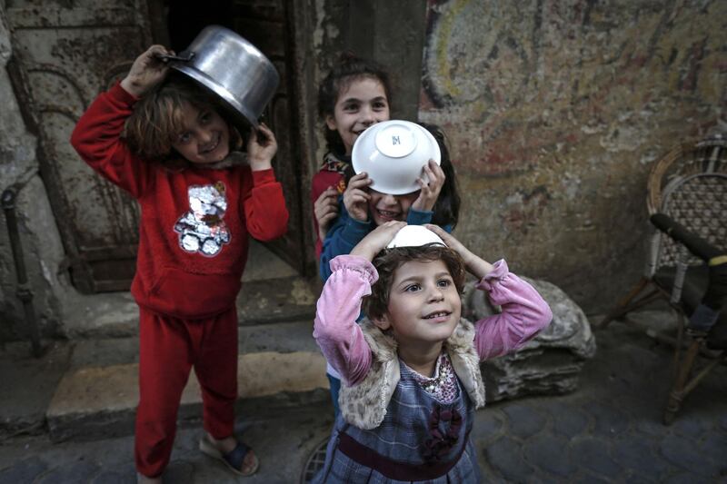 Girls play as Palestinian Walid al-Hattab (unseen) distributes soup to people in need during the Muslim fasting month of Ramadan in Gaza City on April 14, 2021, amid the COVID-19 pandemic. / AFP / Mohammed ABED
