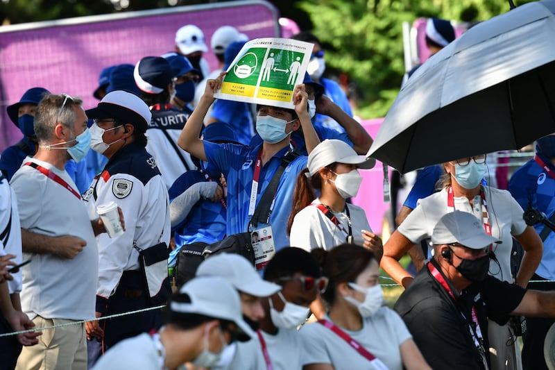 A volunteer holds up a sign to remind people to adhere to Covid-19 protocols during round 4 of the men’s golf individual stroke play during the Tokyo 2020 Olympic Games at the Kasumigaseki Country Club in Kawagoe.