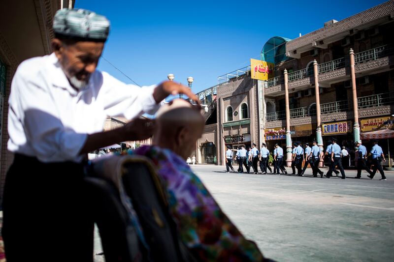 TOPSHOT - This picture taken on June 26, 2017 shows police walking past a barber near the Id Kah Mosque in the old town of Kashgar in China's Xinjiang Uighur Autonomous Region, after the morning prayer on Eid al-Fitr. 
The increasingly strict curbs imposed on the mostly Muslim Uighur population have stifled life in the tense Xinjiang region, where beards are partially banned and no one is allowed to pray in public. Beijing says the restrictions and heavy police presence seek to control the spread of Islamic extremism and separatist movements, but analysts warn that Xinjiang is becoming an open air prison. / AFP PHOTO / Johannes EISELE / TO GO WITH China-religion-politics, FOCUS by Ben Dooley