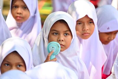 A student uses a portable fan to keep cool while studying outside the classroom during a heatwave at a primary school in Banda Aceh in May. AFP