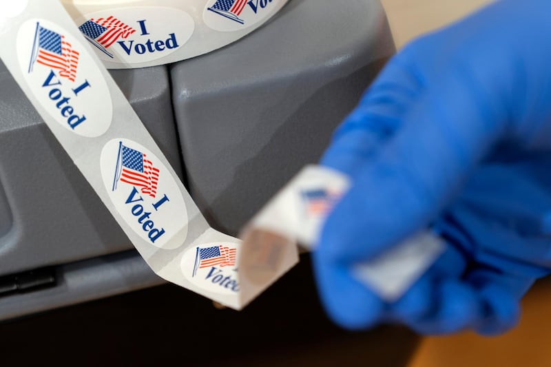 Poll worker Sheila Hawkes removes an "I Voted" sticker to hand to a voter at an early voting center at Ida B. Wells Middle School in Washington. AP Photo