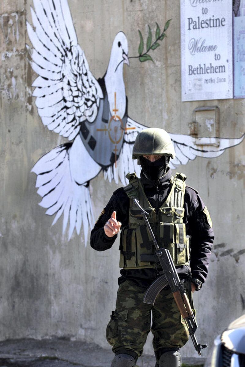 epa07265367 An armed Palestinian policeman stands before a graffiti painting thought to have been painted by the artist known as Banksy that shows a Peace dove wearing a flak jacket with a crosshairs on the bird's chest, painted on a wall at the entrance to the West Bank city of Bethlehem, 06 January 2019. Orthodox believers celebrate Christmas Day on 07 January, according to the Julian calendar.  EPA-EFE/JIM HOLLANDER *** Local Caption *** 54877577