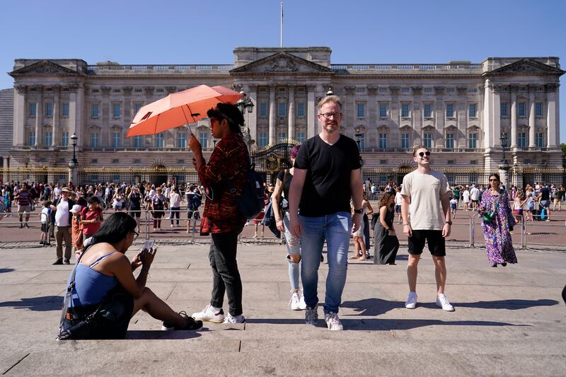 Tourists shelter from the sun as they stand outside Buckingham Palace in London. AP