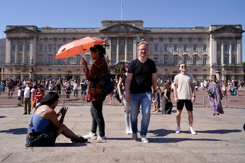 Tourists shelter from the sun as they stand outside Buckingham Palace in London. AP