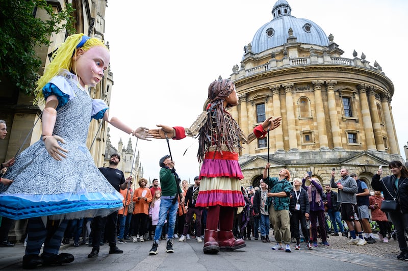Little Amal and Alice in Wonderland greet children in the city centre of Oxford as part of The Walk, a cross-border project highlighting the plight of unaccompanied child refugees. Getty Images