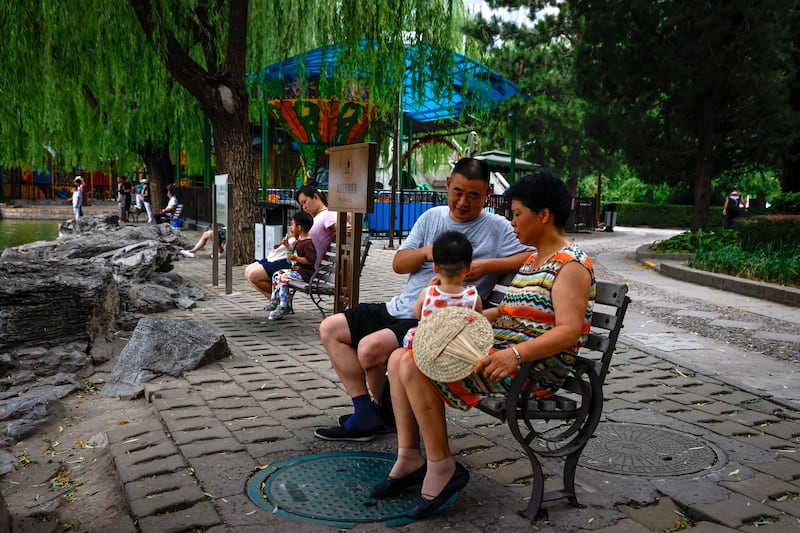 People sit on benches with children at a park in Beijing. EPA