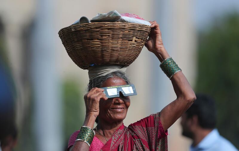 A roadside vendor holds a special filter and watches a partial solar eclipse in Hyderabad, India.  AP