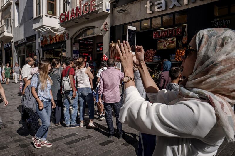 A tourist takes a photograph on a smartphone near a foreign currency exchange store, center, in Istanbul, Turkey, on Monday, Aug. 13, 2018. Turkish policy makers made their first move to bolster the financial system and investor confidence amid a plunge in the lira. The currency, stocks and bonds extended their decline. Photographer: Ismail Ferdous/Bloomberg