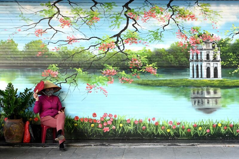 A woman wearing a mask sits outside a closed shop in Hanoi. AFP