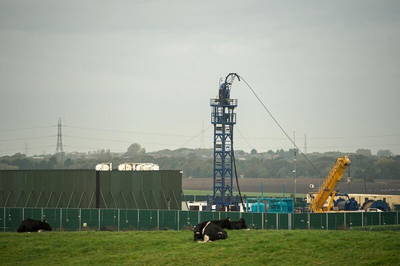 (FILES) In this file photo taken on October 16, 2018 Cows graze in a field as work gets under way at the Preston New Road drill site where energy firm Cuadrilla Resources have commenced fracking (hydraulic fracturing) operations to extract shale gas, near the village of Little Plumpton, near Blackpool, north west England on October 16, 2018. The British government called a temporary halt on November 2 to the controversial process of "fracking" due to fears it could trigger earthquakes. / AFP / OLI SCARFF
