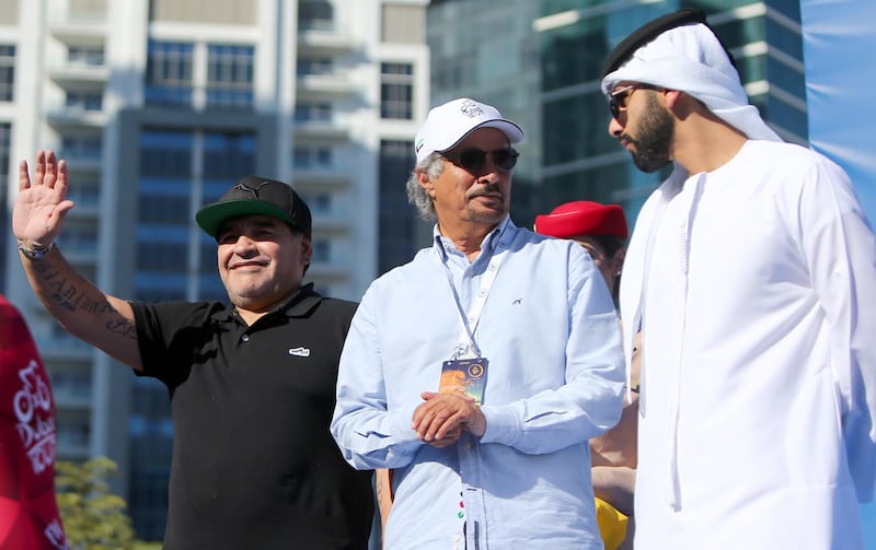 Argentinian legend Diego Maradona (L) waves to crowds as he stands on the podium next to Said Harb (C), Secretary General of the Dubai Sports Council, and Sheikh Mansour, the son of the ruler of Dubai, prior to awarding the winning trophy for the Dubai Tour cycling competition on February 6, 2016 in Dubai. (Photo by MARWAN NAAMANI / AFP)